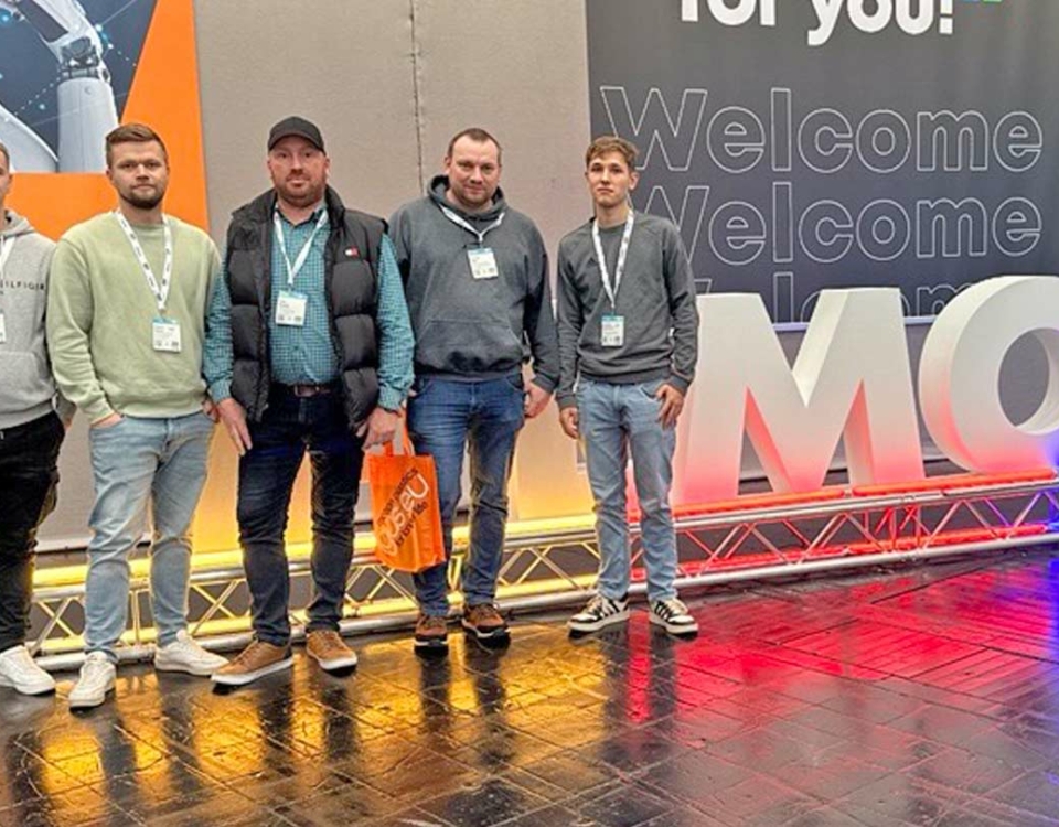 Fünf Männer mit Namensschildern vor großem Messe-Schriftzug in einer Veranstaltungshalle.